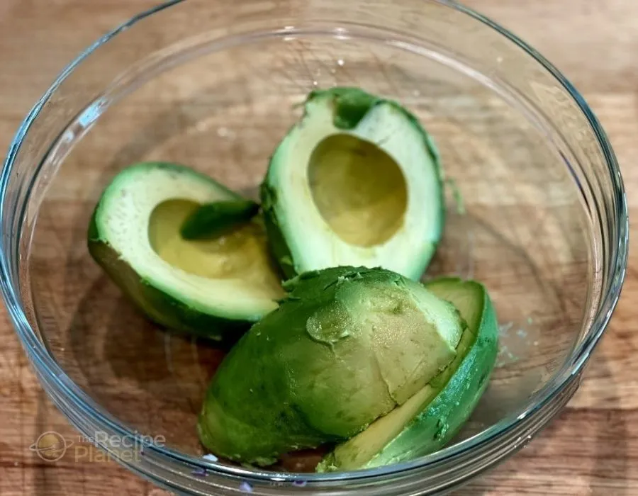 Cut avocados, remove pits, and scoop into a bowl.